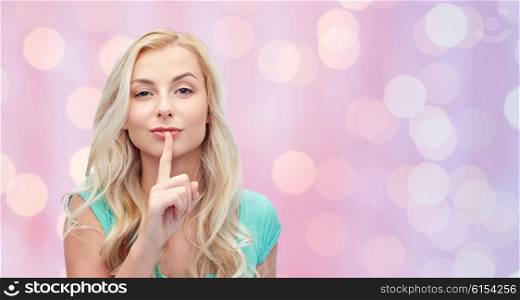 people, gesture and secret concept - beautiful young woman holding finger at her lips over pink holidays lights background