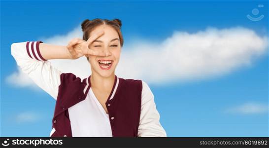 people, gesture and teens concept - happy smiling pretty teenage girl showing peace sign and winking over blue sky and clouds background