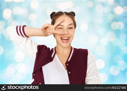 people, gesture and teens concept - happy smiling pretty teenage girl showing peace sign and winking over blue holidays lights background