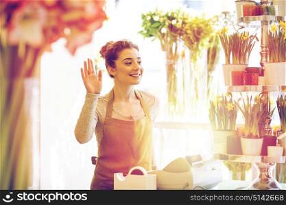 people, gesture, business, sale and floristry concept - happy smiling florist woman waving hand at flower shop cashbox. smiling florist woman at flower shop cashbox