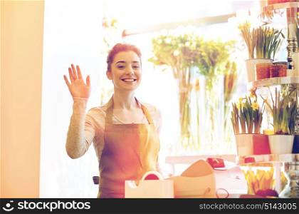 people, gesture, business, sale and floristry concept - happy smiling florist woman waving hand at flower shop cashbox. smiling florist woman at flower shop cashbox