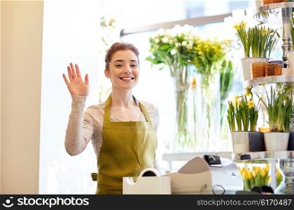 people, gesture, business, sale and floristry concept - happy smiling florist woman waving hand at flower shop cashbox
