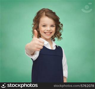 people, gesture, children, school and happiness concept happy little school girl showing thumbs up over green chalk board