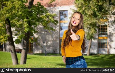 people, gesture, education and fashion concept - happy young woman or teen girl in casual clothes showing thumbs up over campus and summer park background