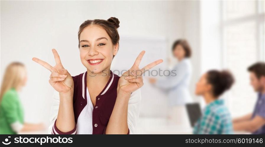 people, gesture, school, education and teens concept - happy smiling student teenage girl showing peace sign over classroom background with teacher and classmates