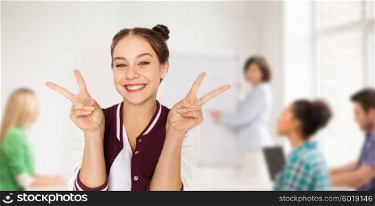 people, gesture, school, education and teens concept - happy smiling student teenage girl showing peace sign over classroom background with teacher and classmates
