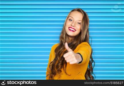 people, gesture, style and fashion concept - happy young woman or teen girl in casual clothes showing thumbs up over blue ribbed background. happy young woman or teen girl showing thumbs up