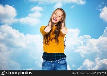 people, gesture, style and fashion concept - happy young woman or teen girl in casual clothes showing thumbs up over blue sky and clouds background