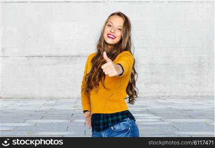 people, gesture, style and fashion concept - happy young woman or teen girl in casual clothes showing thumbs up over urban street background