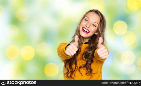 people, gesture, style and fashion concept - happy young woman or teen girl in casual clothes showing thumbs up over summer green lights background