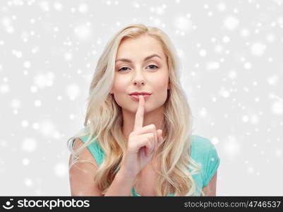 people, gesture, winter holidays, christmas and secret concept - beautiful young woman holding finger at her lips over snow