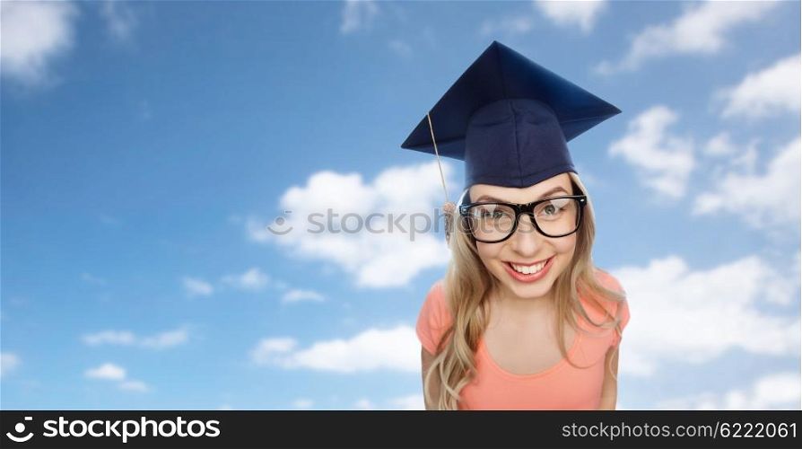 people, graduation and education concept - smiling young student woman in mortarboard and eyeglasses over blue sky and clouds background