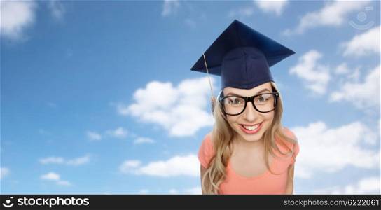 people, graduation and education concept - smiling young student woman in mortarboard and eyeglasses over blue sky and clouds background