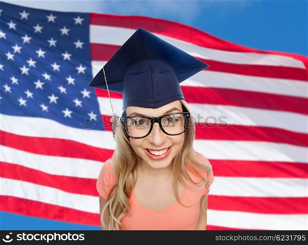 people, graduation and national education concept - smiling young student woman in mortarboard and eyeglasses over american flag background