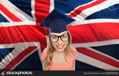 people, graduation and national education concept - smiling young student woman in mortarboard and eyeglasses over english flag