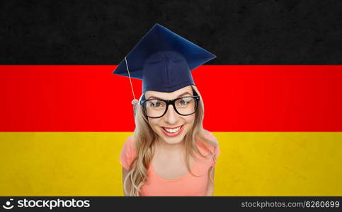 people, graduation and national education concept - smiling young student woman in mortarboard and eyeglasses over german flag background