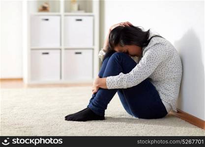 people, grief and domestic violence concept - unhappy woman sitting on floor and crying at home. unhappy woman crying on floor at home