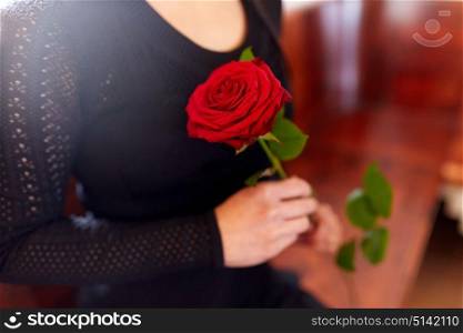 people, grief and mourning concept - close up of woman with red roses sitting on bench at funeral in church. close up of woman with roses at funeral in church