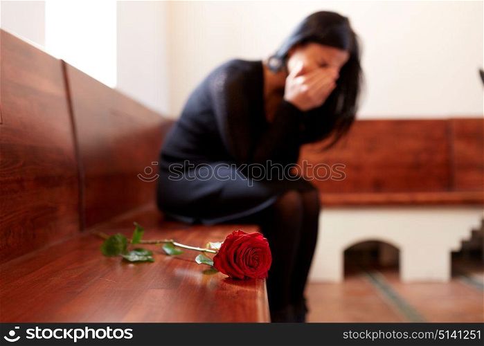 people, grief and mourning concept - crying woman with red rose sitting on bench at funeral in church. crying woman with red rose at funeral in church