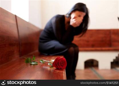 people, grief and mourning concept - crying woman with red rose sitting on bench at funeral in church. crying woman with red rose at funeral in church