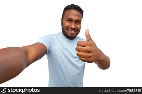 people, grooming and beauty concept - portrait of happy smiling young african american man taking selfie showing thumbs up over white background. smiling young african american man taking selfie