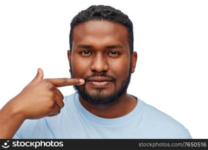 people, grooming and beauty concept - portrait of young african american man pointing finger to his mouth over white background. african american man pointing finger to his mouth