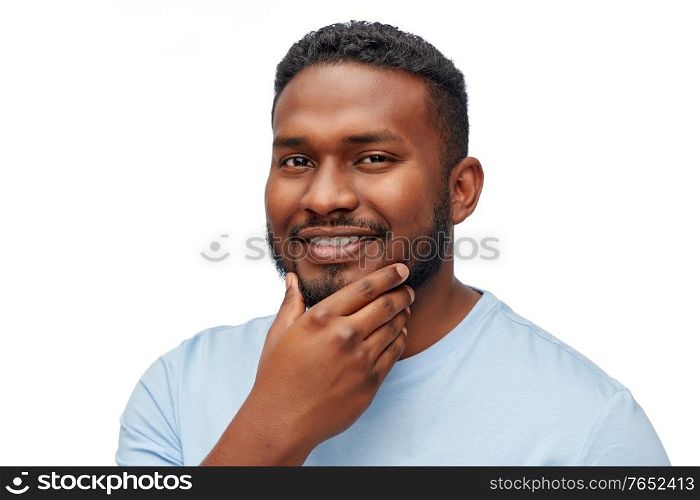 people, grooming and shaving concept - portrait of happy smiling young african american man touching his beard over white background. portrait of smiling young african american man