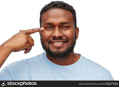 people, grooming and vision concept - portrait of young african american man pointing finger to his eye over white background. african american man pointing finger to his eye