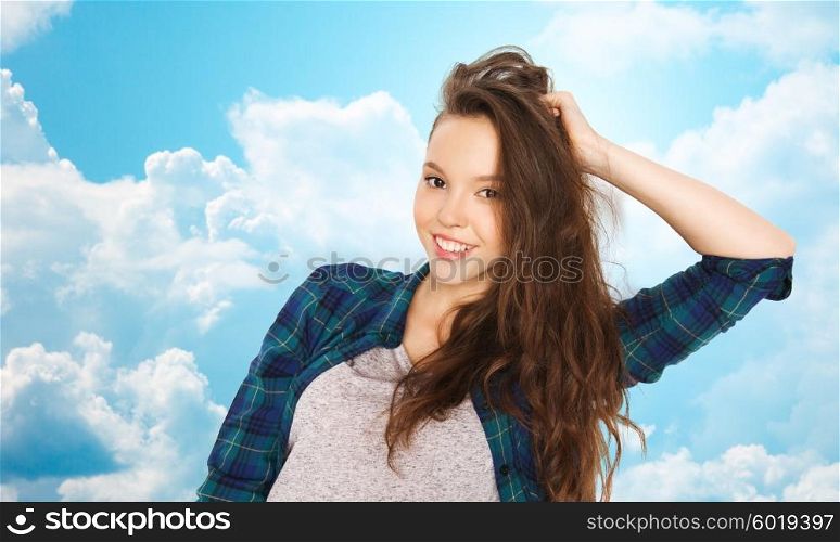 people, hair care, style and teens concept - happy smiling pretty teenage girl touching her head over blue sky and clouds background