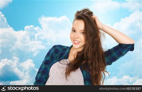 people, hair care, style and teens concept - happy smiling pretty teenage girl touching her head over blue sky and clouds background