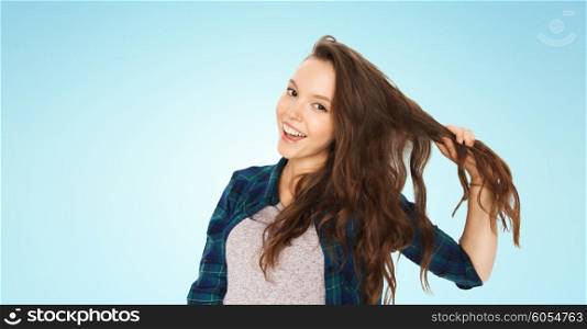 people, hair care, style and teens concept - happy smiling pretty teenage girl holding strand of her hair over blue background