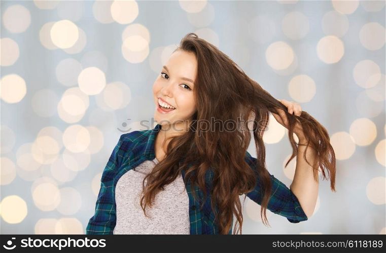people, hair care, style and teens concept - happy smiling pretty teenage girl holding strand of her hair over holidays lights background