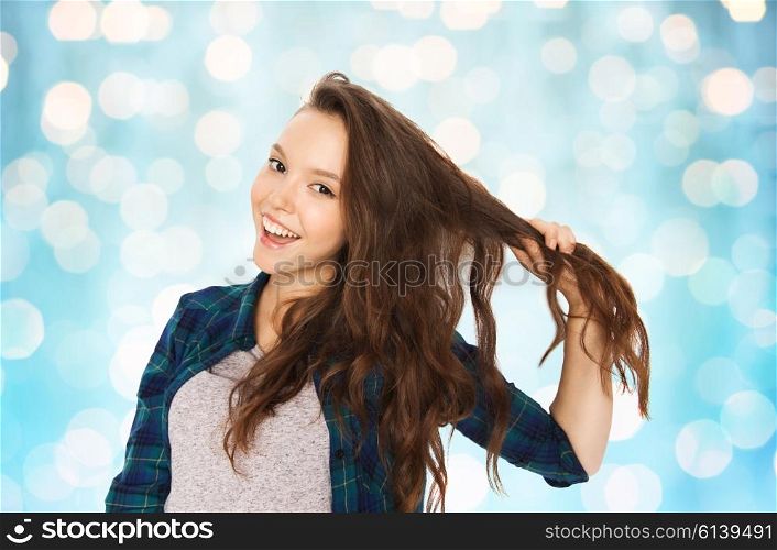 people, hair care, style and teens concept - happy smiling pretty teenage girl holding strand of her hair over blue holidays lights background