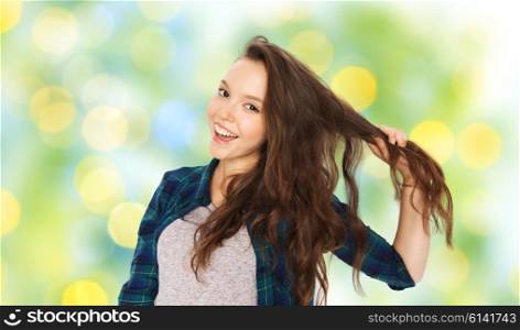 people, hair care, style and teens concept - happy smiling pretty teenage girl holding strand of her hair over green summer holidays lights background