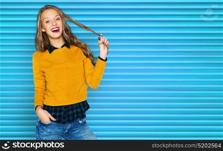 people, hairstyle and fashion concept - happy young woman or teen girl in casual clothes holding her hair strand over blue ribbed background. happy young woman or teen girl in casual clothes