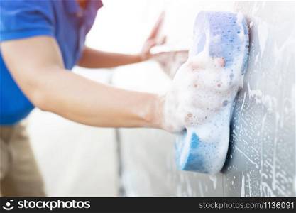 people hand hold blue sponge washing car.