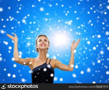 people, happiness, holidays and christmas concept - smiling woman raising hands and looking up over blue snowy background
