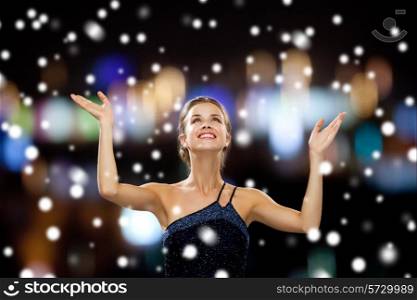 people, happiness, holidays and christmas concept - smiling woman raising hands and looking up over snowy night city lights background