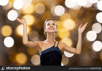 people, happiness, holidays and glamour concept - smiling woman raising hands and looking up over lights background