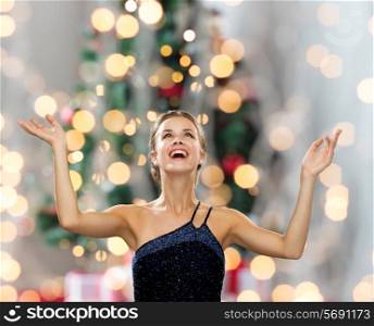 people, happiness, holidays and glamour concept - smiling woman raising hands and looking up over christmas tree lights background