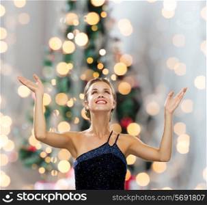people, happiness, holidays and glamour concept - smiling woman raising hands and looking up over christmas tree lights background