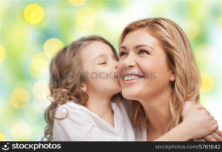 people, happiness, love, family and motherhood concept - happy daughter hugging and kissing her mother over green lights background