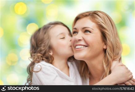 people, happiness, love, family and motherhood concept - happy daughter hugging and kissing her mother over green lights background