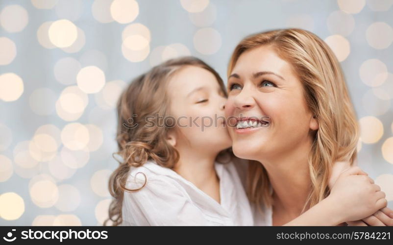 people, happiness, love, family and motherhood concept - happy daughter hugging and kissing her mother over holiday lights background