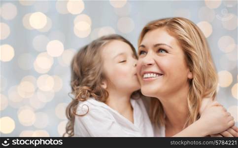 people, happiness, love, family and motherhood concept - happy daughter hugging and kissing her mother over holiday lights background