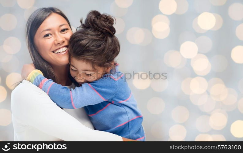 people, happiness, love, family and motherhood concept - happy mother and daughter hugging over holiday lights background