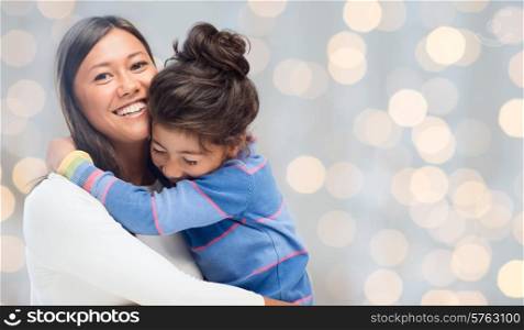 people, happiness, love, family and motherhood concept - happy mother and daughter hugging over holiday lights background