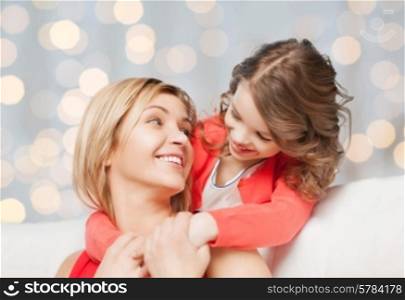 people, happiness, love, family and motherhood concept - happy mother and daughter hugging and talking over holiday lights background