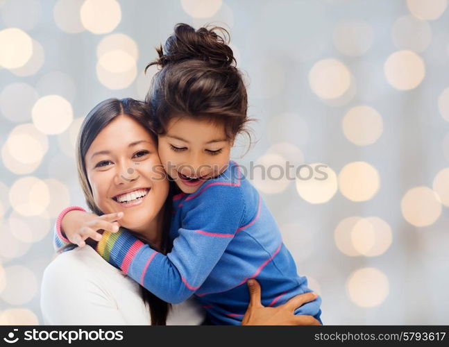 people, happiness, love, family and motherhood concept - happy mother and daughter hugging over holiday lights background