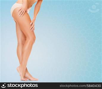 people, health and beauty concept - woman with long legs in cotton panties touching her hips over blue background